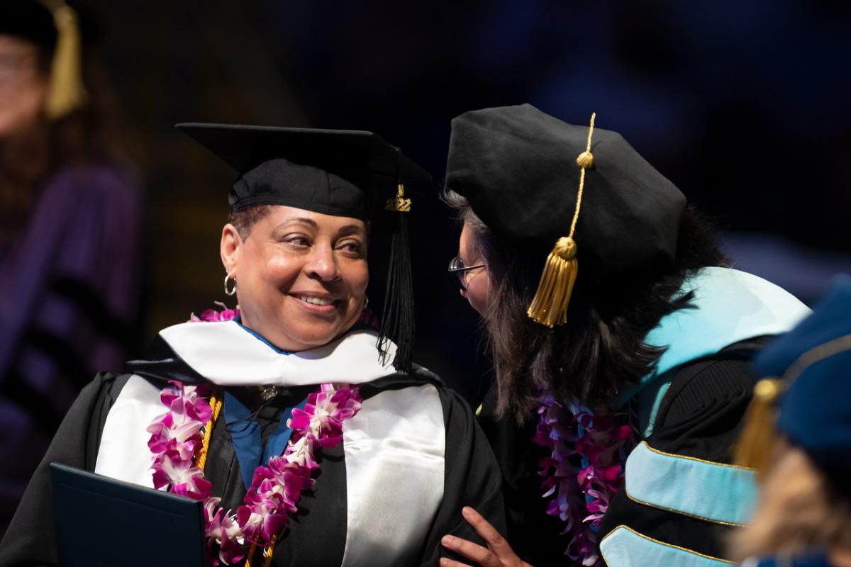 Counseling graduate student at commencement smiling at faculty member.