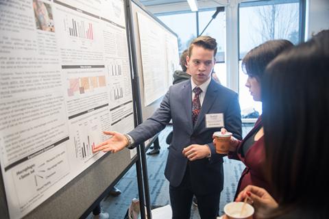 Male student in front of presentation board discussing his research during the CURCA event