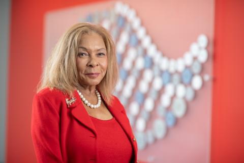 President Linda Thompson of Westfield State. She's wearing a red suit and is posed before a red mosaic wall in the Nettie Stevens Science and Innovcation building