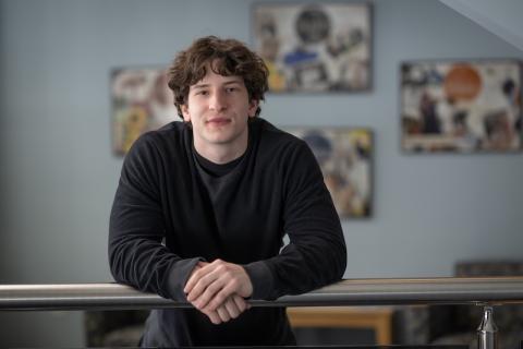 Cole Chapman, health sciences major. He is wearing a black shirt and leans against a railing.