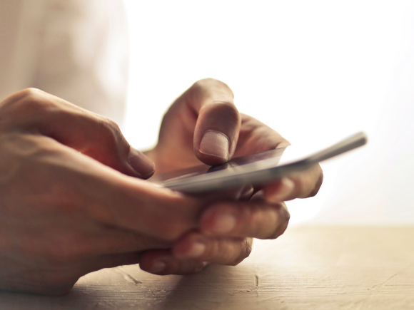 Close up of hands resting on table top holding a smartphone and texting