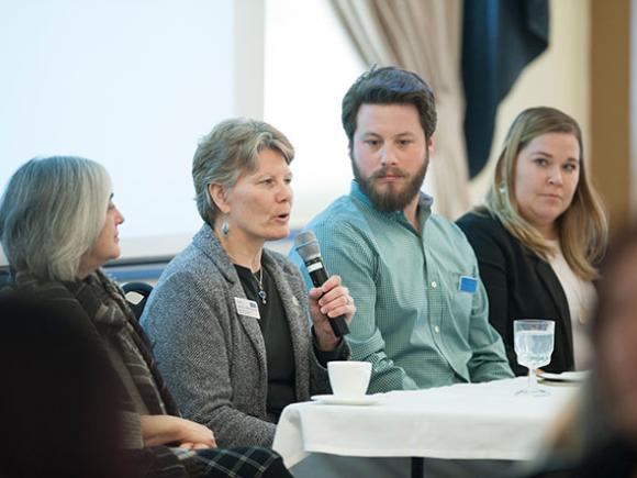 A person speaks into a microphone while other people at the table listen.