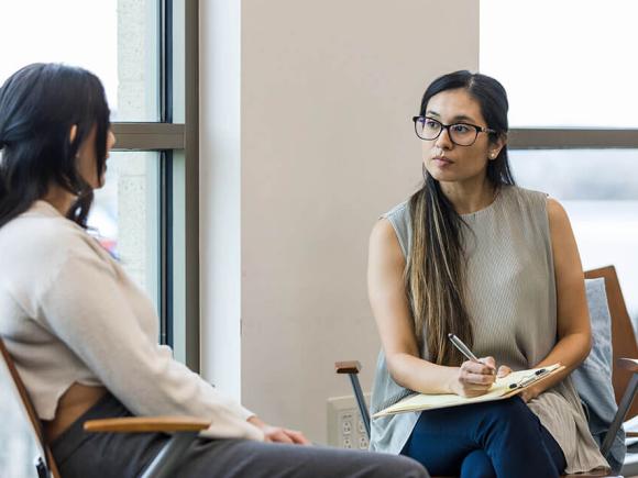 A person takes notes while talking one-on-one with another person.