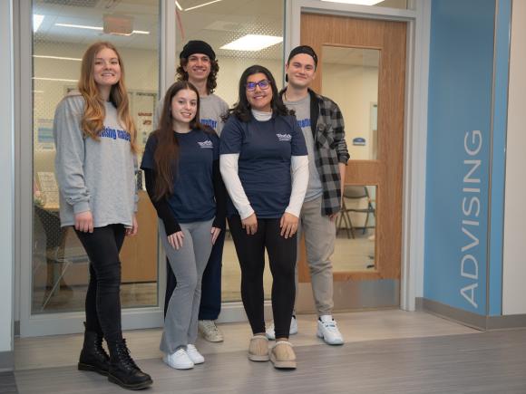 Five students smiling in front of Advising office.