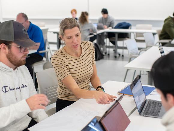 A student and an economics professor sit at a computer while discussing an assignment.