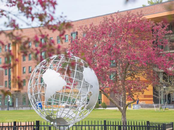 A photo of the campus globe. Two pink-flowered trees are planted on each side.