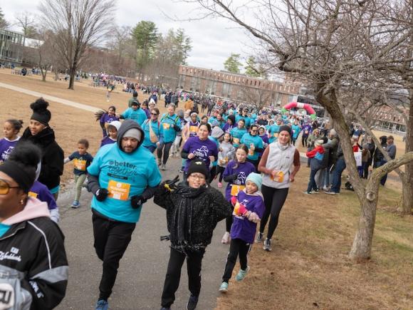 Girls on the Run, hosted on November 24. A crowd of people are running the 5K event in rows, wearing bright blue shirts/