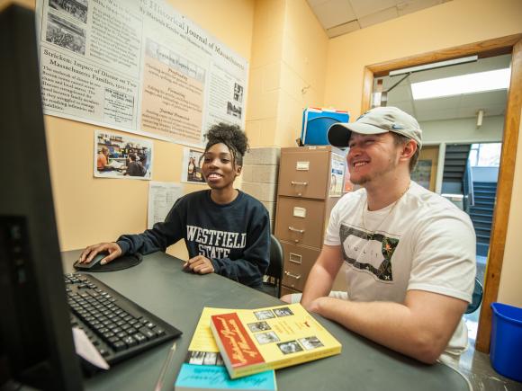 Two students in front of a computer smiling working on a historic journal.