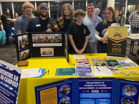 Group of students stand behind the Campus Activities Board table with display posters and handouts 