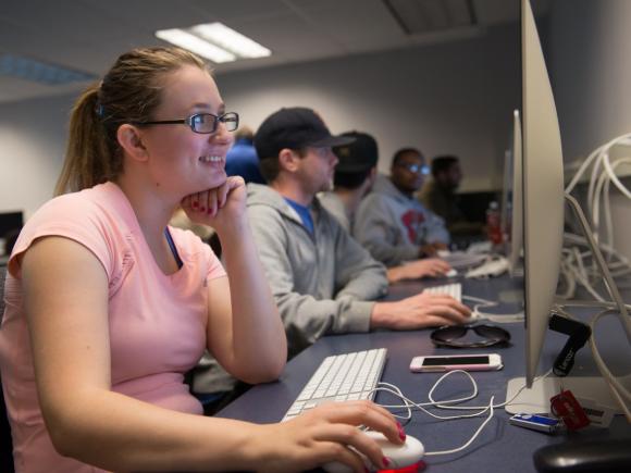 Student smiling at a computer in a web design class.