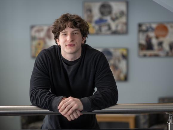 Cole Chapman, health sciences major. He is wearing a black shirt and leans against a railing.