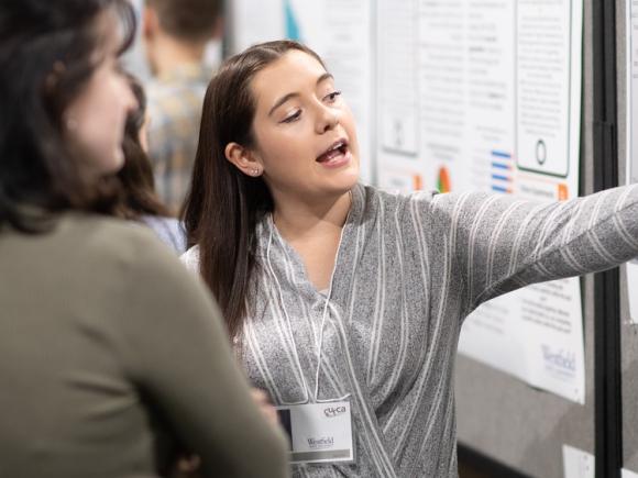 Education student presenting undergraduate research pointing at a poster.