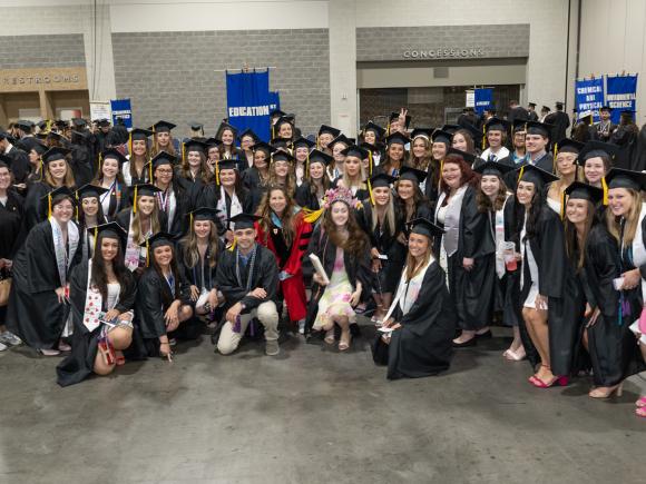 Education undergraduate students at commencement wearing caps and gowns smiling.