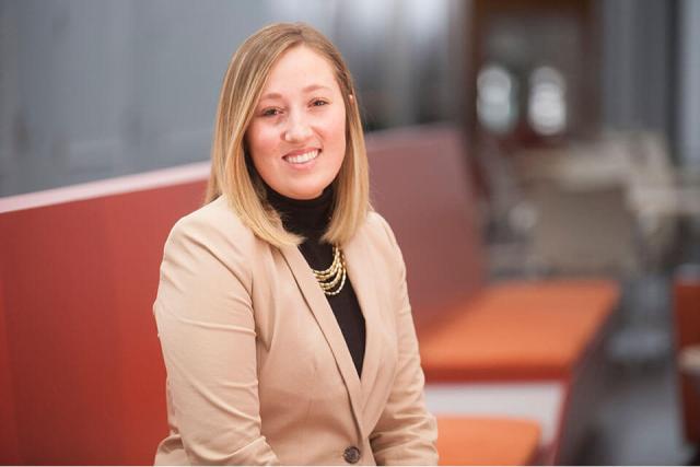 A person wearing a suit is seated on a bench in a lobby setting.