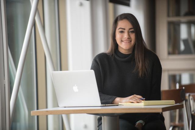 Criminal Justice student in library smiling with laptop