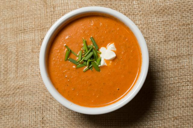 Dining services bowl of tomato soup with green garnish on top.