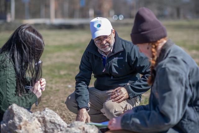 Two students in Earth System Science lab looking at a rock with a faculty member.