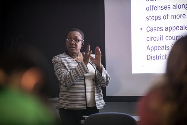 A Criminal Justice professor stands in front of a projection screen while instructing their class of students.