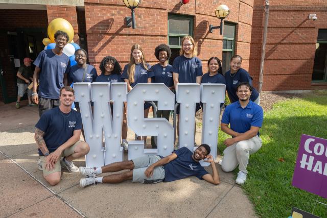 Residence Assistants smiling on the campus green with a WSU sign.