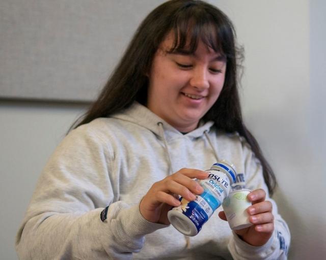 Student in a geriatric lab pouring ensure into a glass.