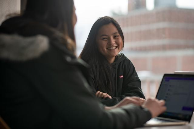 Two students at a laptop smiling.