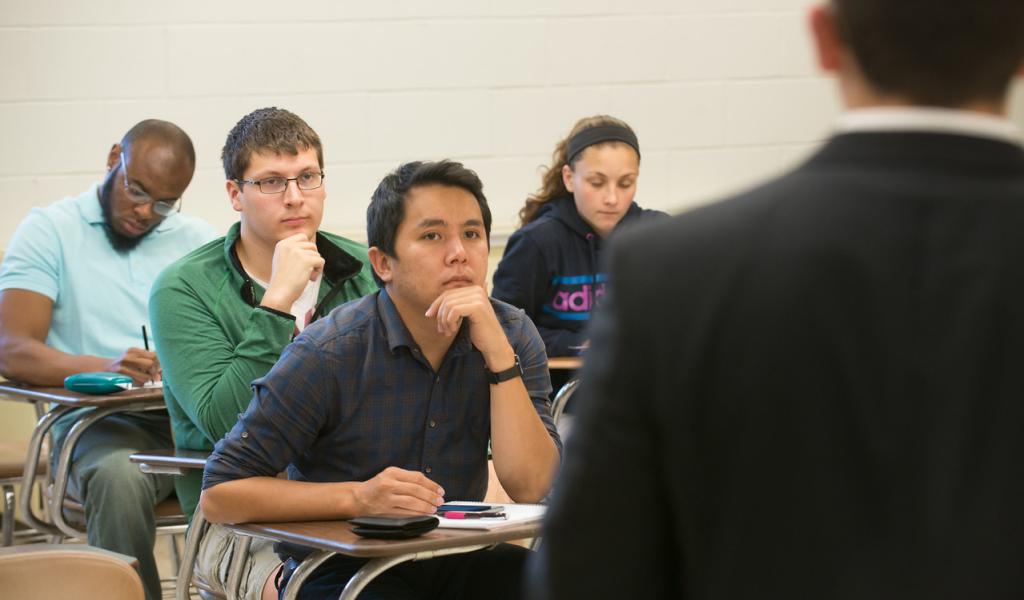 Students in desks watching a man present