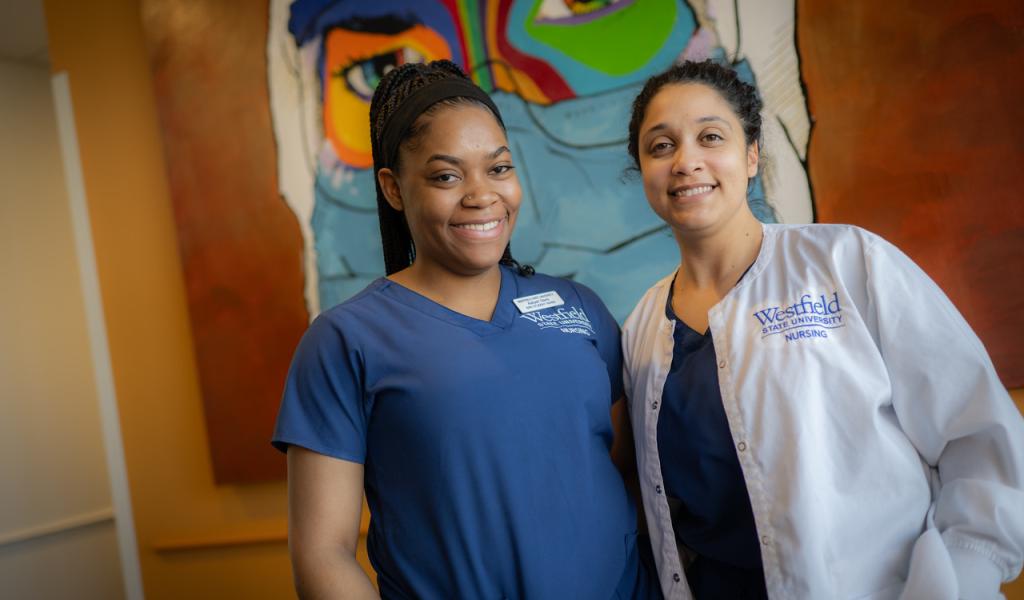 Two smiling nursing students stand in front of a vibrant, colorful mural.