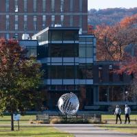 A campus stock photo of the globe and Ely in mid-fall. Red and green trees are on either side of the globe, and two figures are walking in the distance.